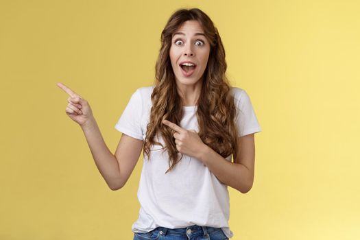 Excellent offer right behind corner. Amused surprised enthusiastic speechless cheering girlfriend scream impressed excited stare camera astonished pointing index fingers left yellow background.
