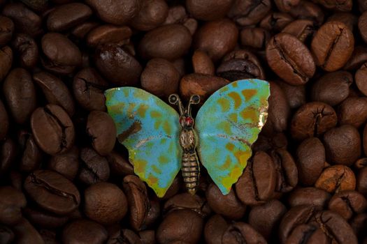A butterfly brooch lies on the scattered coffee beans.