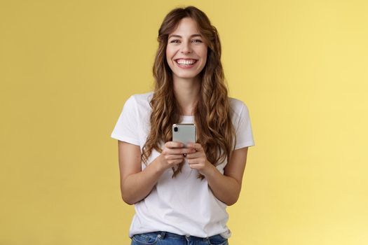Cheerful carefree happy lively girl hold smartphone using awesome funny app playing cool game relaxing waiting friend park browsing social media using mobile phone look camera upbeat smiling. Lifestyle.