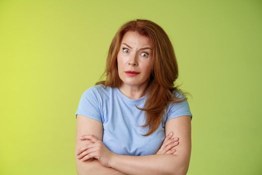 You did what. Confused shocked speechless redhead mature mother stare camera puzzled concerned cross arms chest self-soothing bothered pose look questioned hesitant green background.