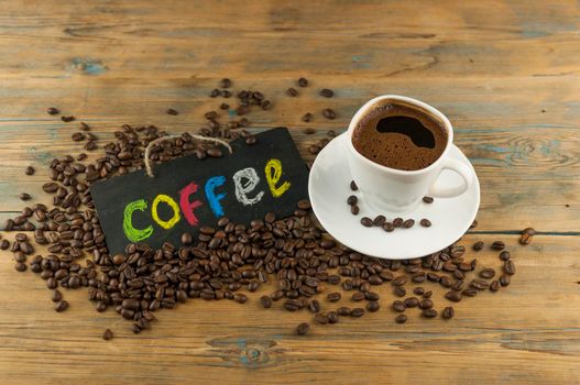 White ceramic cup of coffee and blackboard with inscription "coffee" writen colorful alphabet. Coffee break, morning awakening concept.