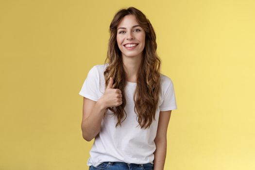 Girl thinks you done great job. Smiling cheerful good-looking woman long curly haircut approve perfect choice give thumb up agree like your style grinning support excellent idea yellow background.