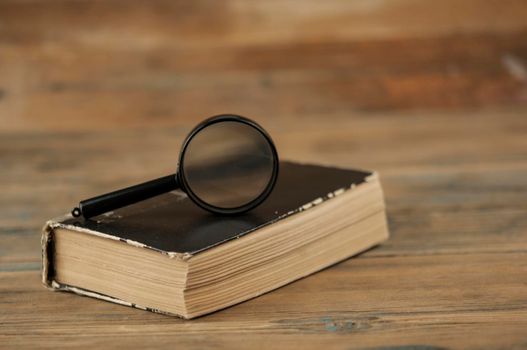 Magnifying glass with close thick old book on wood table 