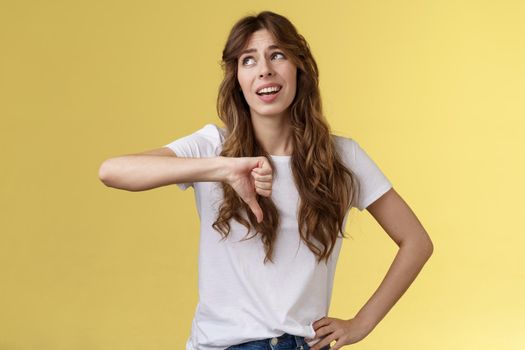 Blah blah boring. Unimpressed apathetic snobbish attractive curly-haired girl look away express scorn disdain show thumb down frowning sharing negative judgement bad opinion yellow background.
