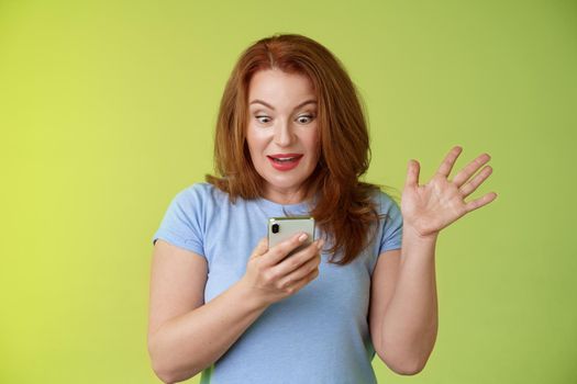 Surprised enthusiastic happy redhead mature middle-aged woman. receive excellent message read perfect news social media hold smartphone stare astonished pleased mobile phone screen raise hand triumph.