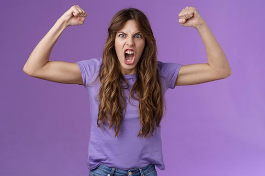 Funny curly-haired girl raising hands fist pump show muscles yelling daring cool shouting encouraged motivated win grimacing strong powerful woman celebrating victory feel like champion. Lifestyle.