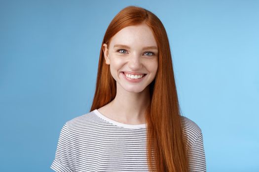 Pleasant reliable sincere good-looking redhead female freelancer college student make confident professional impression smiling broadly assertive helpful standing blue background self-assured.