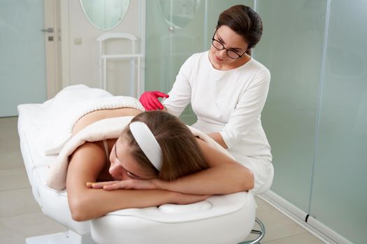 Young woman getting fat reductive skin lifting body treatment by cosmetologist. Attractive female patient enjoying slimming body contouring procedure