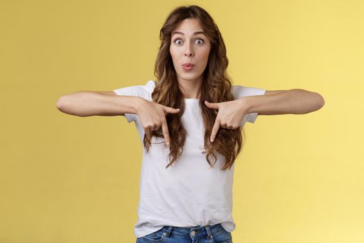 Fascinated impressed charismatic brunette female curly long haircut folding lips whistle astonished react excited thrilled telling you incredible promotion pointing down bottom yellow background.