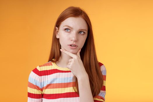 Smart creative serious-looking redhead female coworker thinking deep focus pondering idea making choice touching chin thoughtful look upper left corner questioned puzzled orange background.