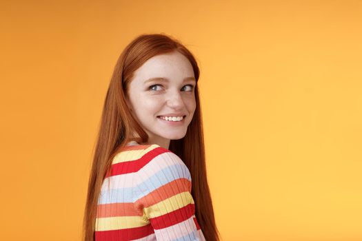 Tender romantic carefree european redhead girlfriend turning behind look left amused smiling pleased coquettish gaze standing orange background flirty romantic mood wanna receive date invitation.