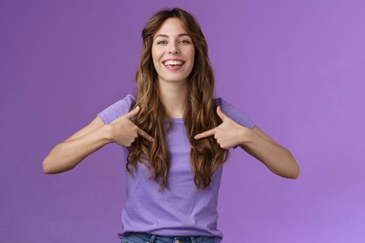 Boastful good-looking curly european female pointing herself proud who she is grinning delighted coming out pride month smiling broadly indicating center chest bragging purple background. Lifestyle.