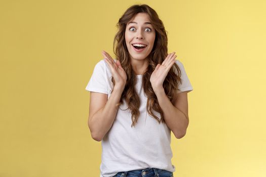 Surprised happy pleased impressed curly-haired girl gaze camera admiration satisfaction joy clap hands cheerful smiling broadly look camera fascinated enthusiastic applause yellow background.