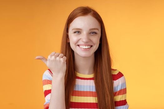 Girl pointing left cool person can help smiling delighted look friendly camera discuss interesting project introduce friend during conversation standing happy grinning orange background.