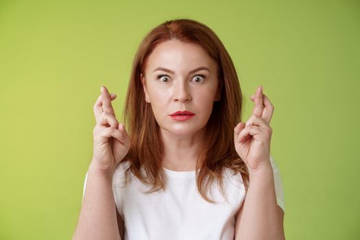 Stunned intense worried middle-aged redhead woman. stare nervously awaiting important result implore dream come true receive positive reply standing stupor green background make wish good luck.