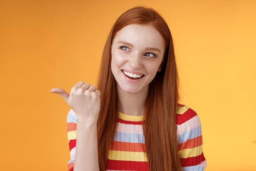 Amused outgoing redhead stylish female student discuss girly things smiling cheeky pointing handsome guy smirking devious pointing thumb looking intrigued curiously staring orange background.