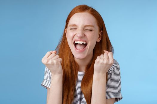 Yes achievement goal lifetime. Smiling happy european redhead girl raising clenched fists cheerful rejoicing yelling yeah accomplish goal success triumphing victory, great news win lottery.