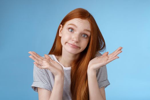 Lifestyle. Unsure clueless cute silly redhead female part-time worker shrugging careless raise hands unaware smirking tilting head lift eyebrows confused cannot answer no idea standing blue background.