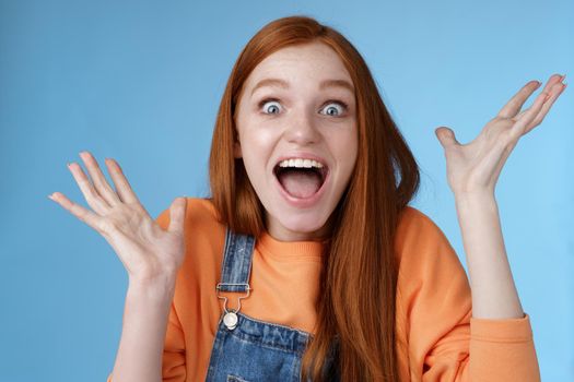 Surprised astonished sensitive overwhelmed young happy redhead girl receive incredible fantastic prize wide eyes astonished raising hands triumphing win lottery celebrating joyfully.