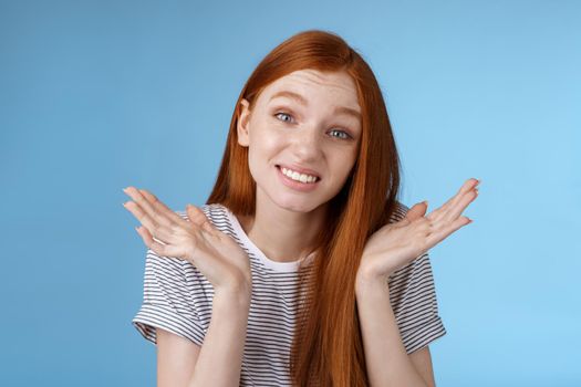 Awkward apologizing cute redhead girlfriend say sorry shrugging spread hands sideways puzzled smiling uncomfortably standing clueless unaware forgetting meeting, posing blue background.