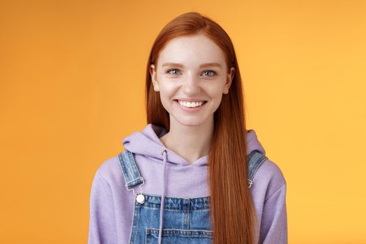 Attractive modern hipster young redhead girl smiling delighted relaxed talking have casual joyful day downtown walking friends wearing purple hoodie overalls, summer vibes, standing orange wall.