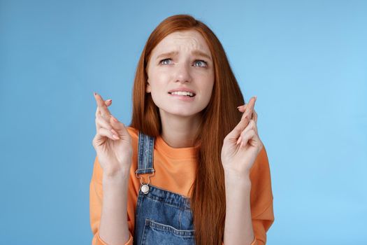 Lifestyle. Worried unconfident young redhead intense cute girl frowning nervously waiting improtant moment cross fingers good luck bite lip anxiously frowning look upper left corner praying wish come true.