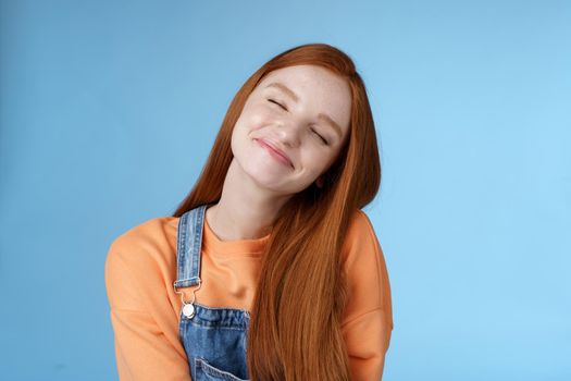 Dreamy kind silly redhead smiling happy girl straight long ginger hair daydreaming imagine romantic moment close eyes smiling delighted tilting head look joyful, standing blue background.