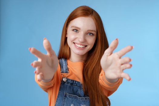 Come into arms. Charming sincere happy kind redhead girl baby sitting stretch hands camera wanna hold catch smiling friendly asking pass object, standing blue background reach friend give cuddles.