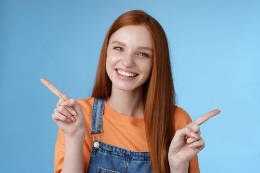 Friendly happy laughing pretty redhead girl female student showing lots opportunities advice make choice pointing sideways left right introducing different product grinning gladly, blue background.