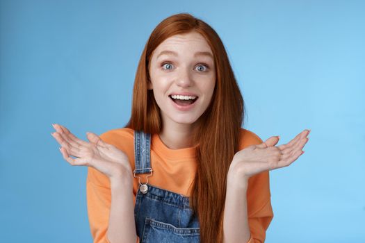 Lifestyle. Amused surprised glad young redhead girl speechless happy see friend came back hometown wide eyes impressed grinning raise hands sideways full disbelief standing blue background joyful.