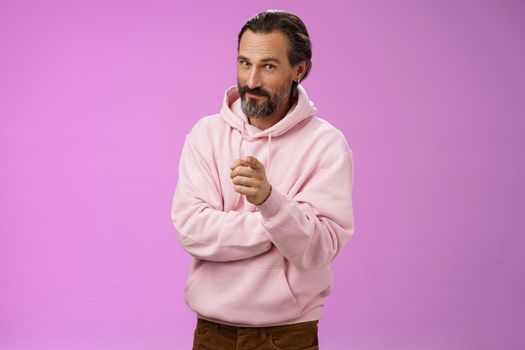 Confident handsome charismatic adult bearded man in stylish pink hoodie inviting you join company smiling self-assured indicating picking make decision chosing us, purple background.