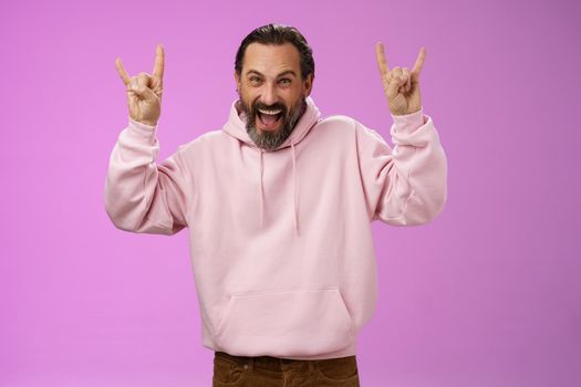 Carefree enthusiastic excited mature bearded man grey hair having fun show rock-n-roll gesture attend awesome heavy metal concert grimacing thrilled looking happy upbeat, purple background.