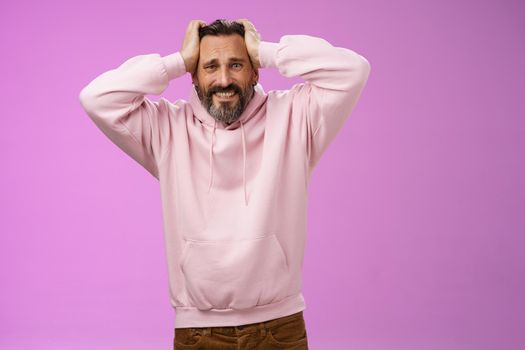 Adult worried insecure bearded man panicking despair touch head clenching teeth bothered anxiously looking camera troubled standing concerned have problems bad feeling, standing purple background.