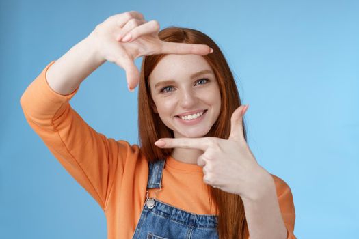 Creative good-looking nice redhead female assistant searching inspiration make hand frame look through delighted smiling satisfied found great spot take shot standing blue background.