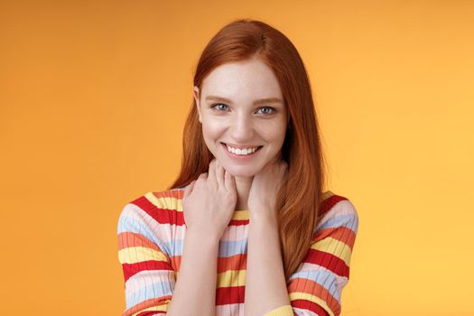 Pleased happy tender feminine redhead gorgeous girl blushing flirty giggle gazing camera smiling broadly touching neck modesy shy sensually talking guy likes standing orange background silly. Lifestyle.