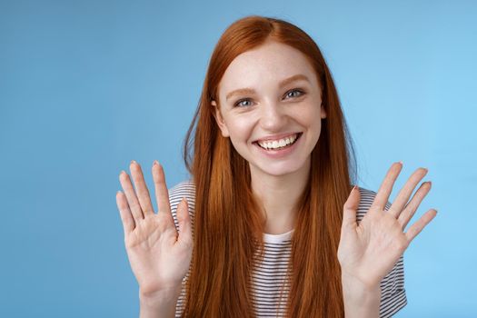 Charming redhead elder sister say goodbye sibling friends smiling cheerful waving raised palms show ten fingers grinning joyfully look carefree relaxed, talking casually blue background.