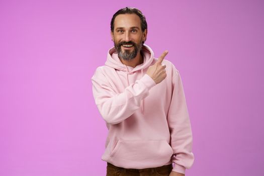 Good-looking lucky energized happy mature 50s man grey hair in trendy hipster hoodie pointing upper right corner amused telling you interesting news smiling white teeth thrilled joyfully look camera. Lifestyle.