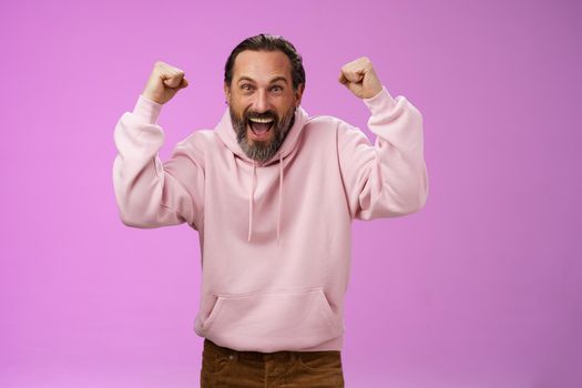 Excited cheering devoted male bearded grey hair yelling supportive words win lottery place good lucky bet standing pleased triumphing say yes raising fists victory success gesture, purple wall.