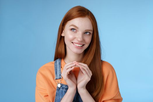 Devious tricky smart pretty redhead girlfriend have evil plan smirking mysteriously look upper left corner twiddles fingers think excellent plan, smiling delighted, standing blue background.