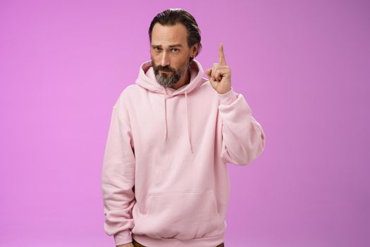 Strict serious-looking stylish bearded father teaching scolding teenage son raising index finger frowning displeased disappointed bad child behaviour, make statement, standing purple background.