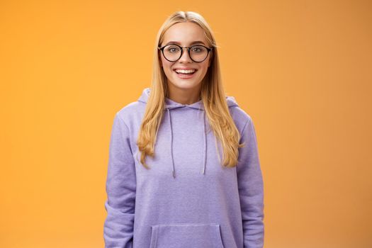 Charming female student geek smiling energized wanna participate university event grinning look excited wearing glasses purple hoodie standing amused orange background having fun. Copy space