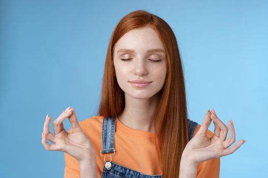 Keep calm redhead relaxed girl stay relieved positive close eyes smiling delighted raising hands sideways lotus mudra gesture practice yoga meditation do breathing exercise, blue background.