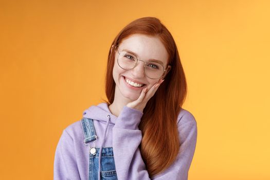 Smiling satisfied happy redhead girl get rid acne delighted touching soft clean skin laughing joyfully talking feel confidence self-assured own beauty, standing orange background enjoy communication.