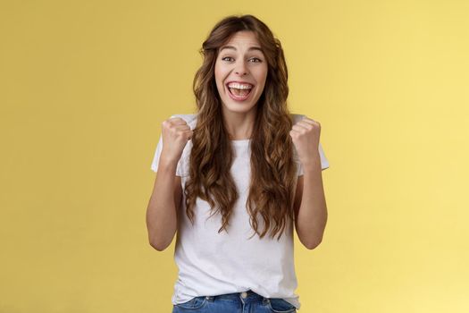 Yes finally success. Cheerful enthusiastic happy girl pump fists lift hands victory joy celebration gesture smiling broadly relieved winning lottery amused stand yellow background triumphing.