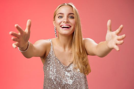 Hospitable charming nice young blond woman wanna hug come closer camera extend arms welcoming embracing cuddling being clingy smiling delighted standing amused red background. Copy space