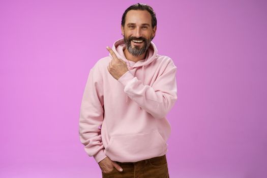 Charming friendly happy mature man 50s bearded grey hair laughing happily pointing upper left corner behind showing proudly family members standing purple background having fun stay positive. Lifestyle.