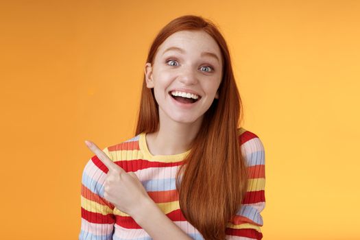 Amused carefree thrilled emotional redhead female fan adore talking favorite movie pointing upper left corner fascinated smiling broadly happy delighted attend incredible party, orange background. Lifestyle.