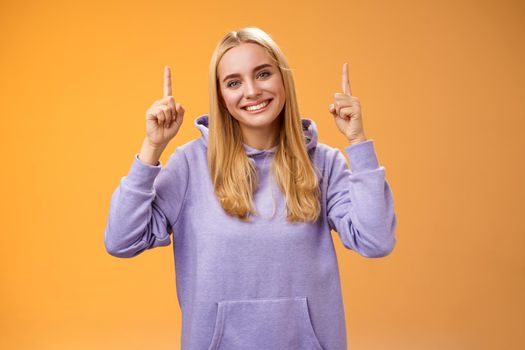 Helpful friendly-looking supportive charming female friend pointing up showing awesome new product advertisement suggesting check out tilting head gladly smiling help out, orange background.