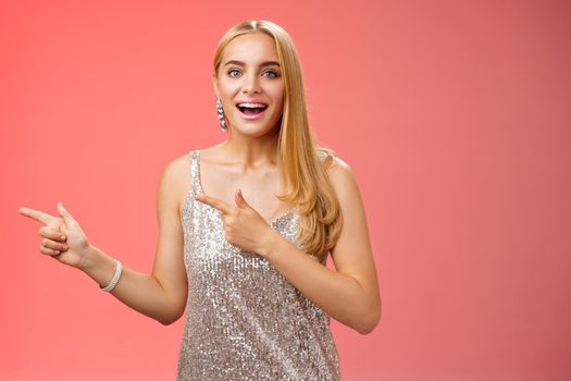 Lifestyle. Excited carefree happy young attractive woman joyful attend awesome party in silver beautiful glittering dress pointing left suggesting come together inviting dance smiling cute red background.