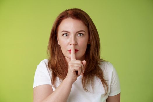 Hush not say that. Worried shocked redhead middle-aged wife demand keep mouth shut shushing ask silence stop spread false rumours stare camera hold index finger pressed lips taboo gesture.